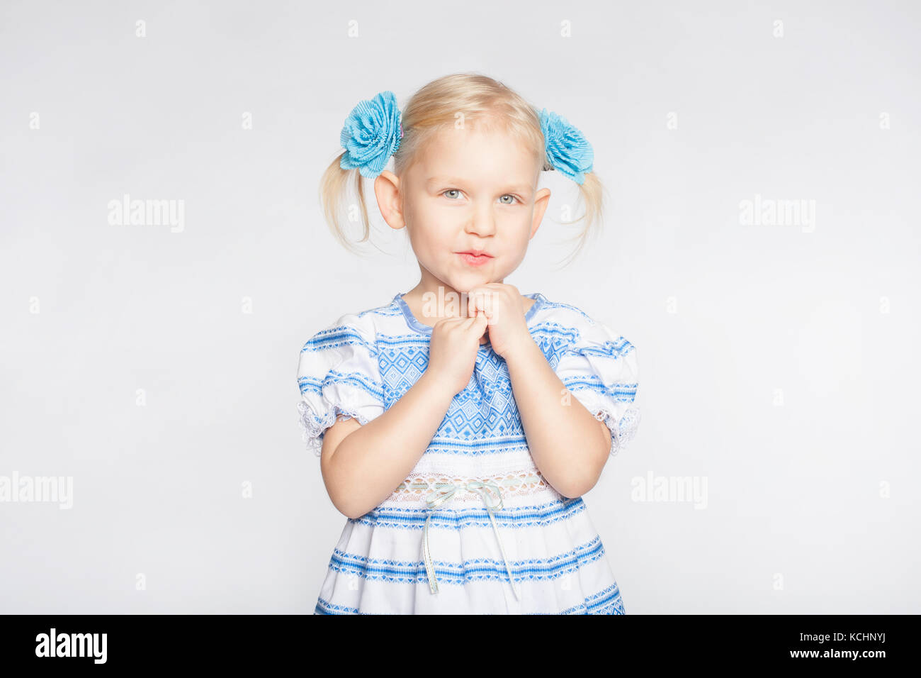 Kleine Blonde Mädchen auf einem weißen Hintergrund, der mit gefalteten Händen Stockfoto