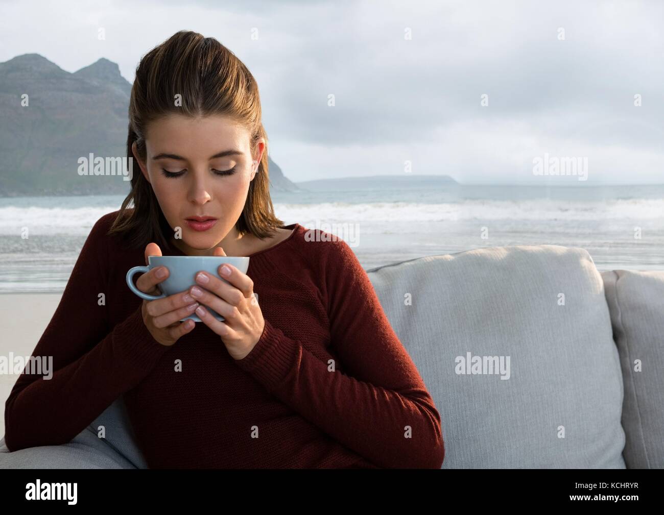 Digital composite von Frau trinkt aus der Schale auf dem Tisch mit Meerblick Berglandschaft Stockfoto