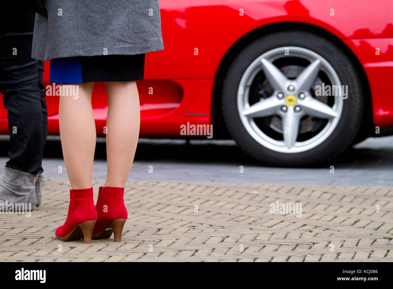 Europa, Niederlande, Südholland, Delft, Frau mit roten Halbschuhen vor einem roten Ferrari auf dem Marktplatz. Europa, Niederlande, Südholl Stockfoto
