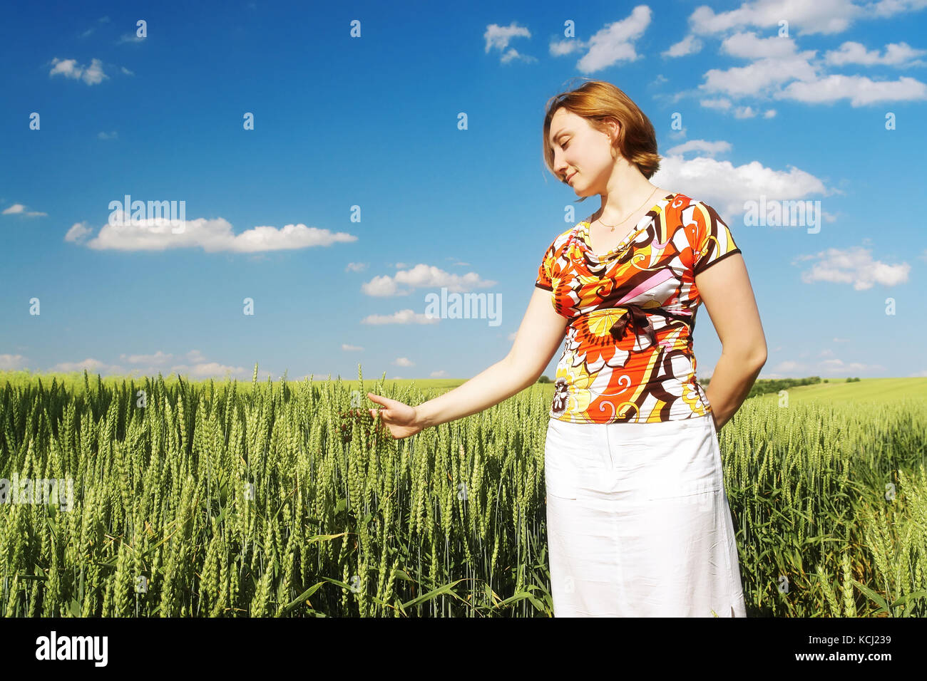 Verträumte Mädchen mit Blumen geschmückten Bluse und weißen Rock stehen in Weizen cornfield zart berühren Mais Ohren mit ihren Handflächen Stockfoto