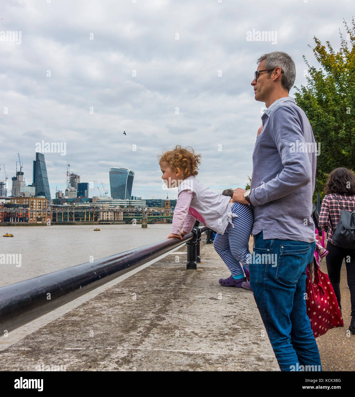 Einen mittleren gealterten Vater hielt seinen lockigen Haaren junge Tochter, greifen einen Sicherheitsbügel, mit Blick auf die Themse, South Bank, London, England, UK. Stockfoto