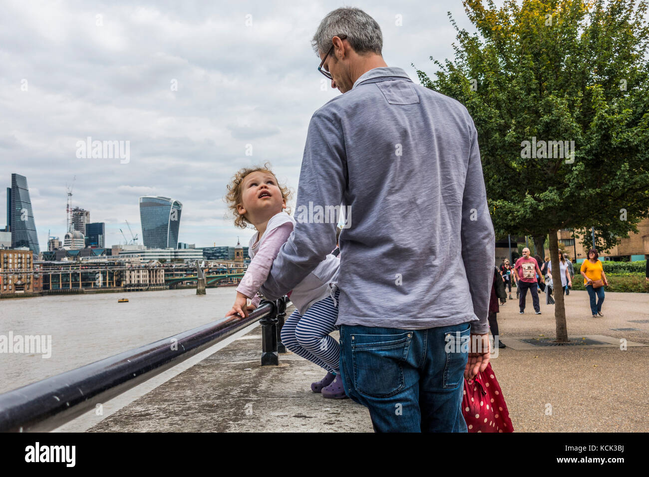 Einen mittleren gealterten Vater hielt seinen lockigen Haaren junge Tochter, greifen einen Sicherheitsbügel, mit Blick auf die Themse, South Bank, London, England, UK. Stockfoto