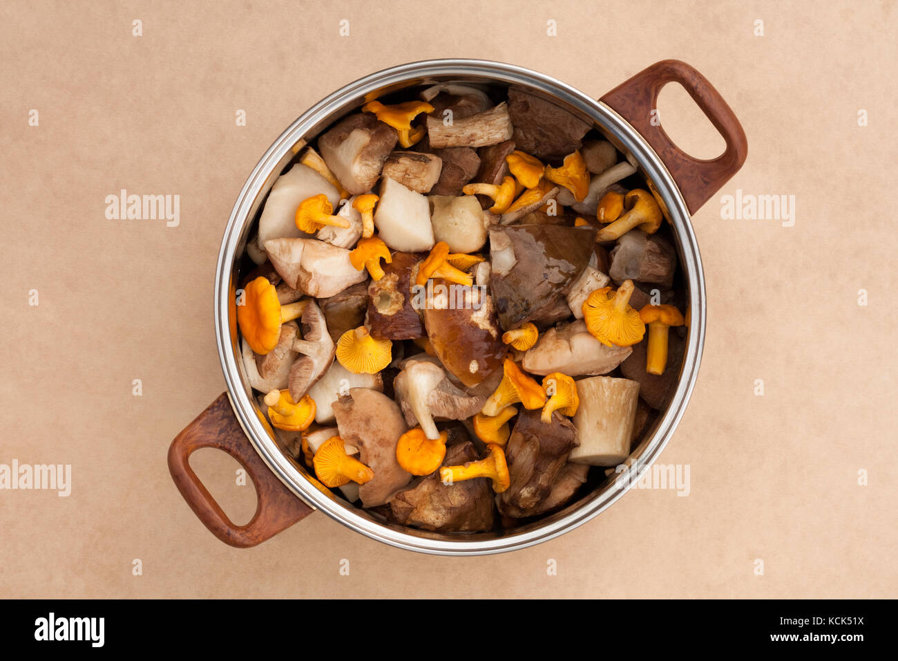 Rohe Frische Speisepilze Chanterelles Und Sauber Geschnittenes Porcini In Large Metal Kitchen Pot Pan Auf Beigefarbenem Braunem Hintergrund Top View. Stockfoto