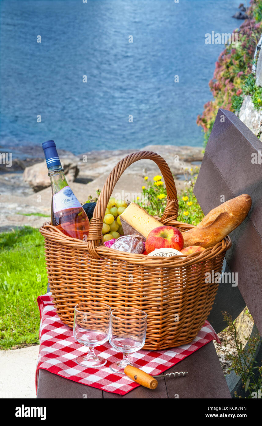 Typisch französischer Picknickkorb mit Roséwein, Baguette, Käse usw. im Hafen von Doelan, Finistere Brittany France Stockfoto