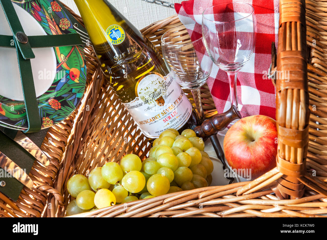 Picknickvorbereitungen mit einer Flasche Muscadet sur Lie Weißwein im Picknickkorb mit typischen karierten Tischdecken Gläsern und Korkenzieher Stockfoto