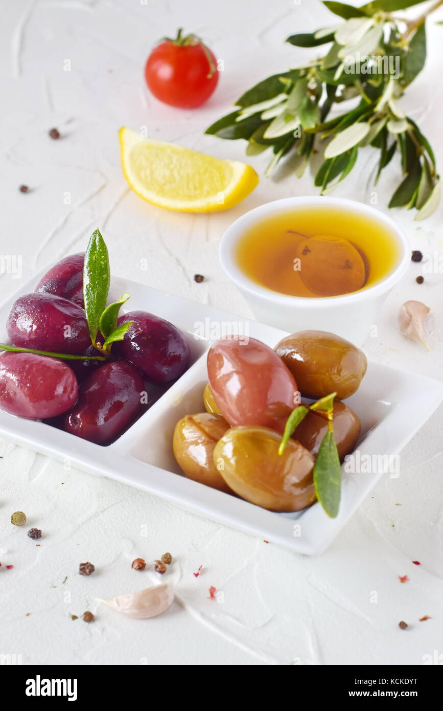 Weiße Platte mit schwarze und grüne Oliven mit Oliven Blätter auf einem weißen Abstrakt Hintergrund mit Zitrone, Cherry Tomaten, Gewürze. gesundes Essen. griechisches Essen. Stockfoto