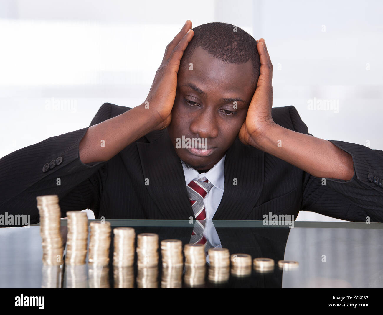 Portrait von sorgen junge afrikanische Unternehmer auf der Suche nach Münzen Stapel auf dem Schreibtisch Stockfoto