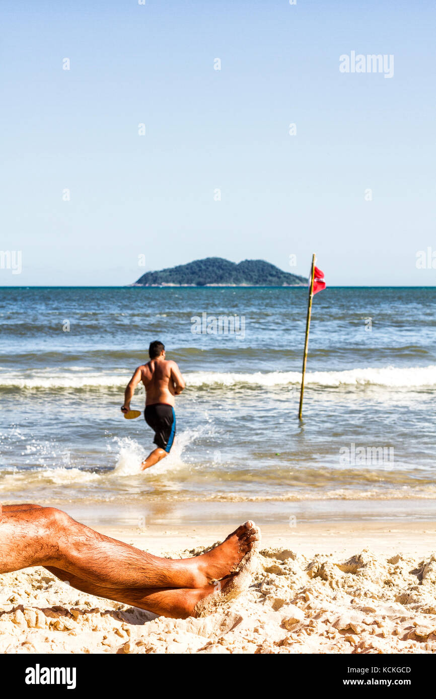 Gestreckte Beine eines Mannes auf dem Sand am Acores Beach. Florianopolis, Santa Catarina, Brasilien. Stockfoto