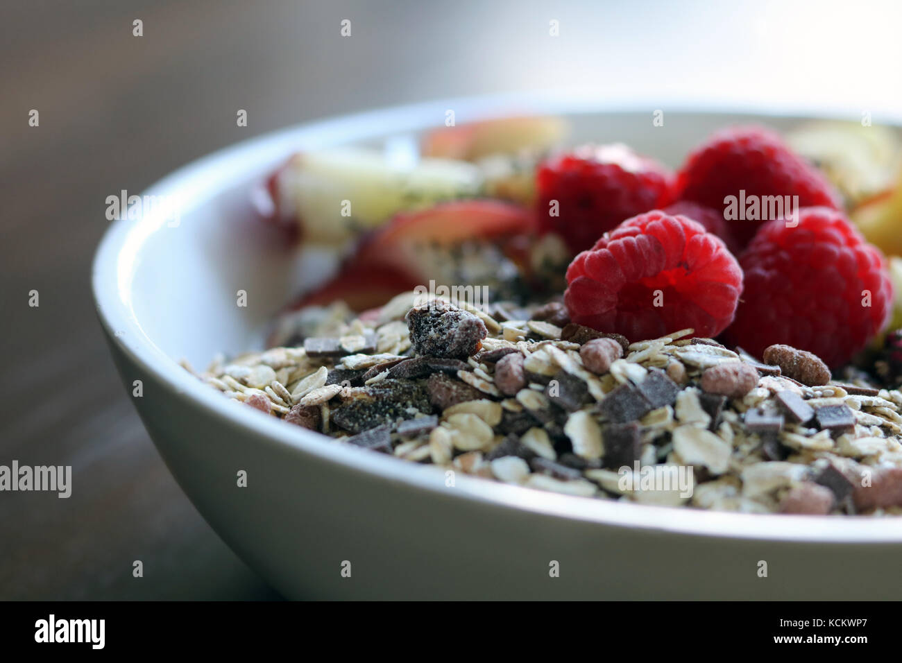 Gemischtes Obst und Müsli in einer weißen Schüssel auf braune Holztisch Stockfoto