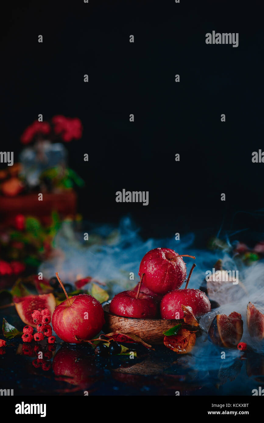 Kleine rote Äpfel auf einer Holzplatte in einem Herbst noch Leben mit Blättern und Rauch. dunklen Essen Fotografie mit kopieren. Stockfoto