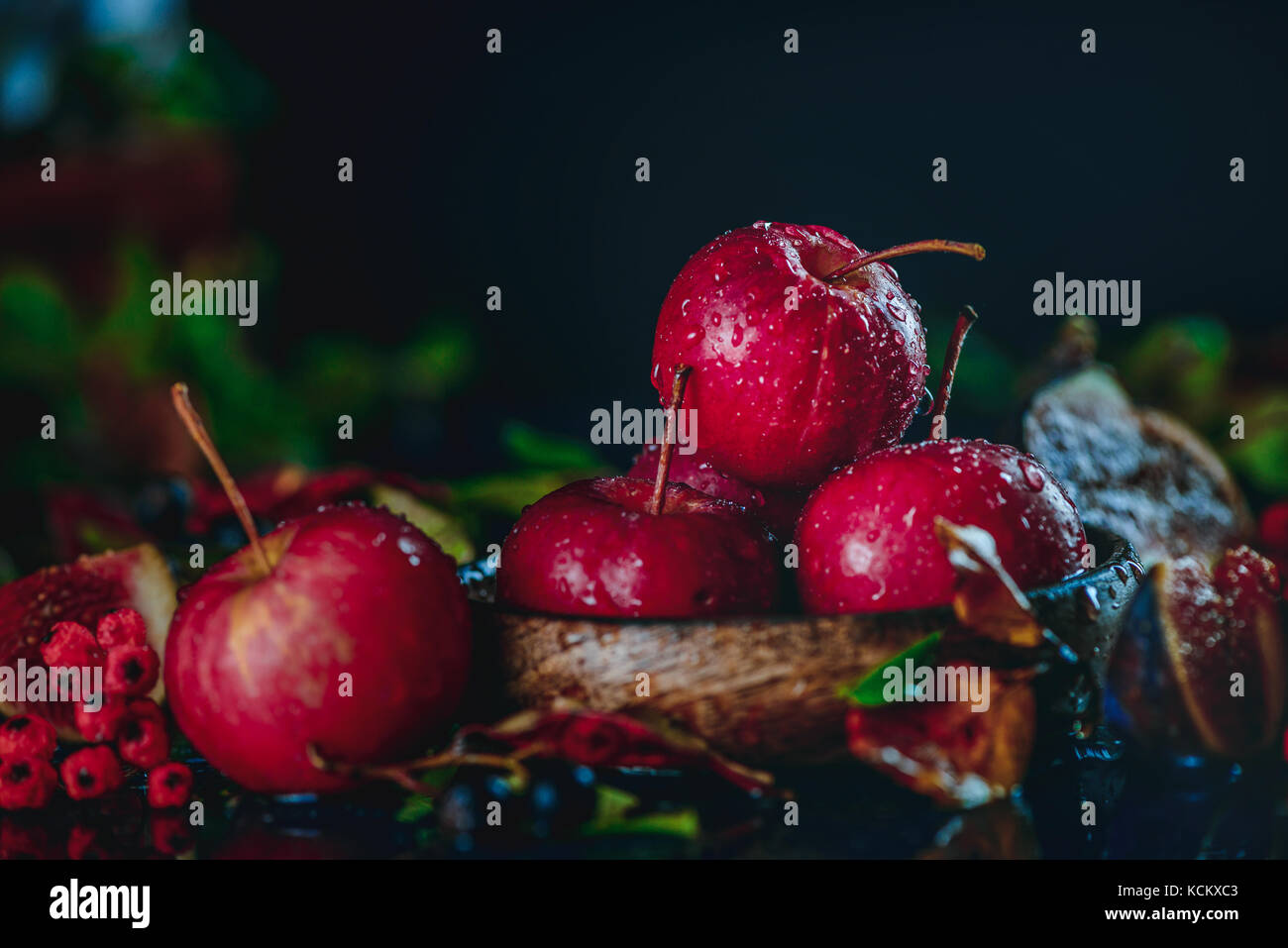 Rot miniatur Äpfel Close-up in einem Herbst noch Leben mit Laub. Dunkle essen Fotografie mit kopieren. Ernte Konzept Stockfoto