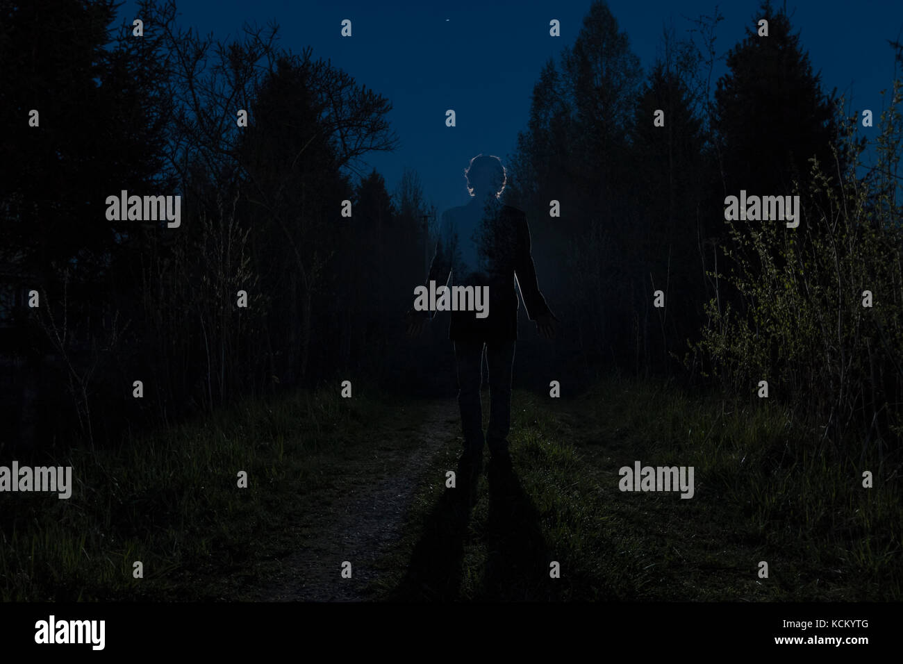 Männliche Silhouette in den dunklen Wald Weg durch die Büsche in der Nacht. Mann auf der Straße gegen die Autoscheinwerfer. Geheimnis ghost Konzept Stockfoto