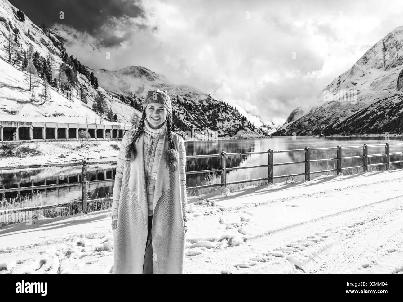 Winter auf höherer Ebene Spaß. Portrait von lächelnden Elegante reisenden Frau gegen Berglandschaft mit See in Alto Adige, Italien Stockfoto