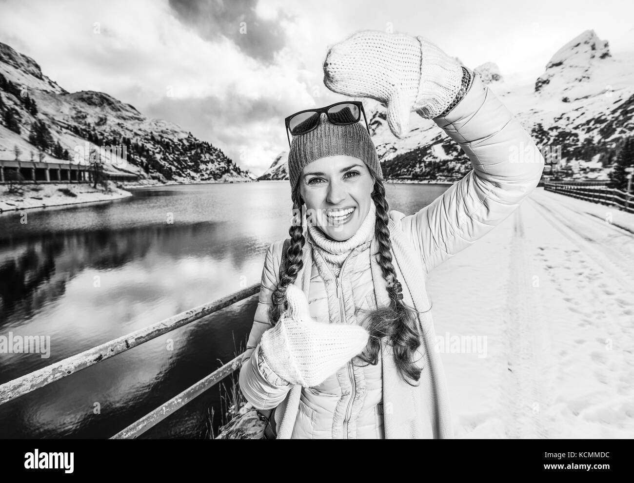 Winter auf höherer Ebene Spaß. Portrait von lächelnden modernen Reisenden Frau gegen Berglandschaft mit See in Alto Adige, Italien mit Händen Framing Stockfoto