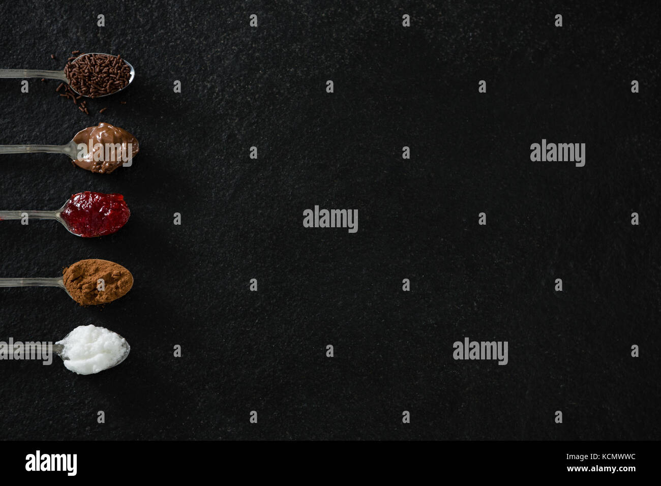 Verschiedene cookies Würzen Zutaten in Löffel auf schwarzem Hintergrund Stockfoto