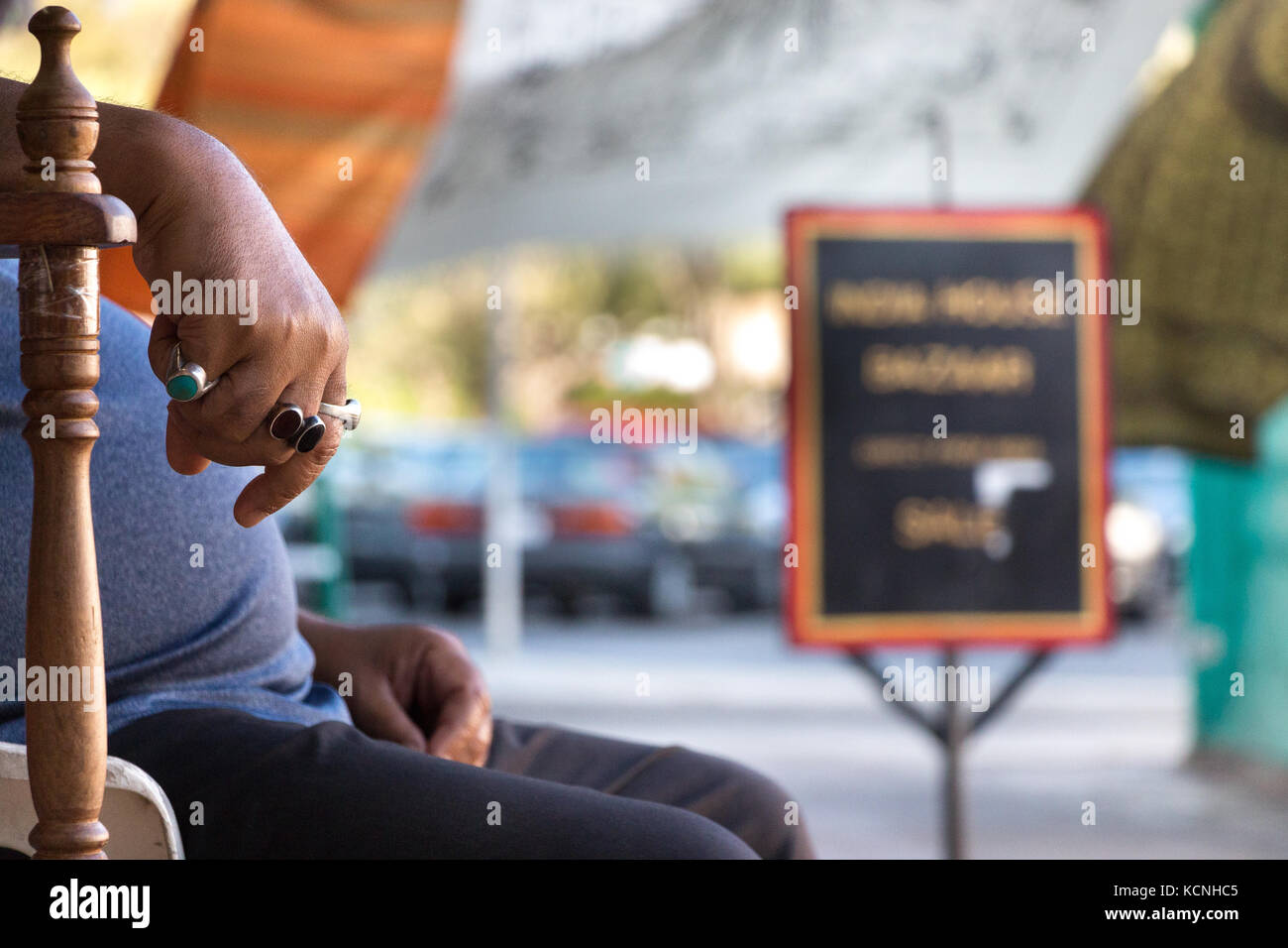 Eine männliche Hand, indische Ethnizität tragen Ringe auf einer hölzernen Armlehnen Stuhl, im Freien. Stockfoto