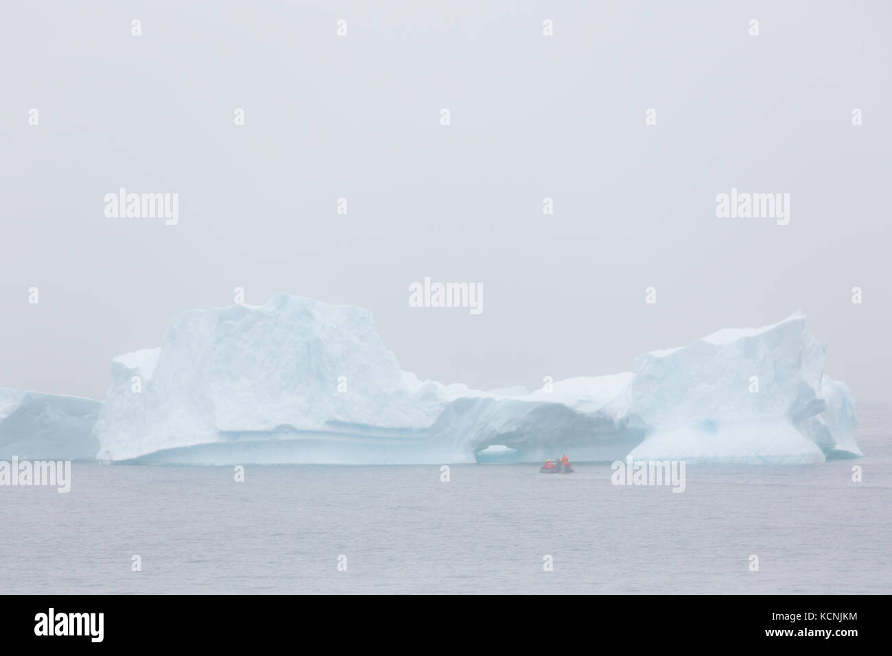 Sanfte Beleuchtung beleuchtet einen großen Eisberg und Zodiak in der Gerlache-Straße. Antarktische Halbinsel Stockfoto