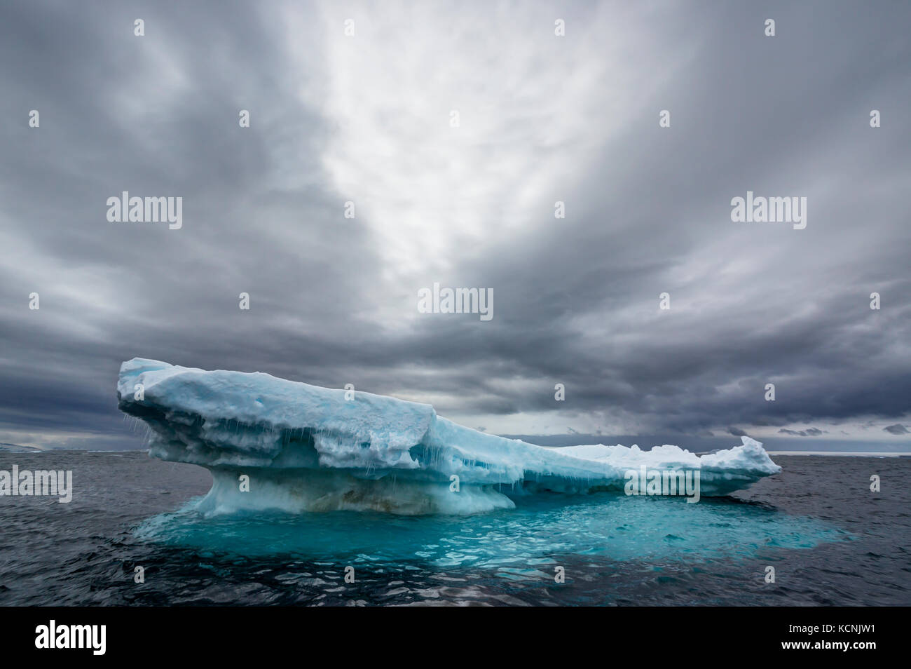 Ein schwimmender Eisberg weicht langsam dem unvermeidlichen Ansturm des Ozeans unter einem dramatischen Himmel nahe Joinville Island, Antarktische Halbinsel, Antarktis Stockfoto