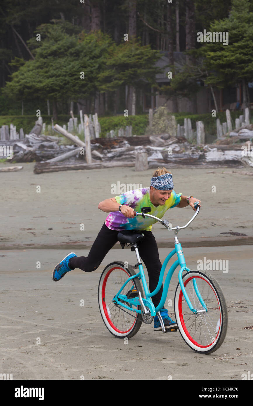Ein Reiter mit einem tie dye t-shirt spielt auf seinem Beach Cruiser während auf Chesterman Beach. Tofino, Vancouver Island, British Columbia, Kanada. Stockfoto