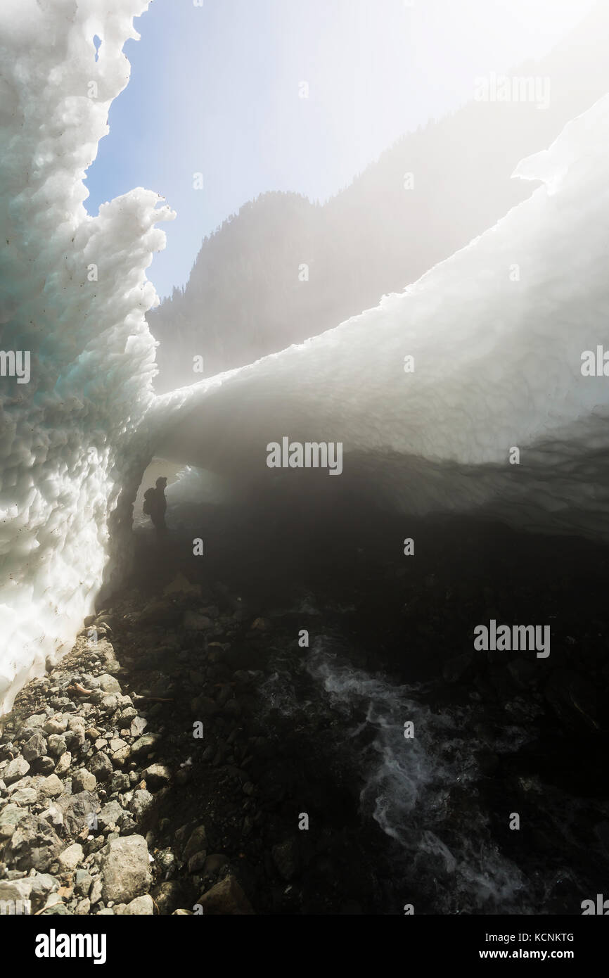 Ein Wanderer schaut auf eine Schneehöhle am Fuße des Century Sam Sees. Strathcona Park, Vancouver Island, British Columbia, Kanada Stockfoto