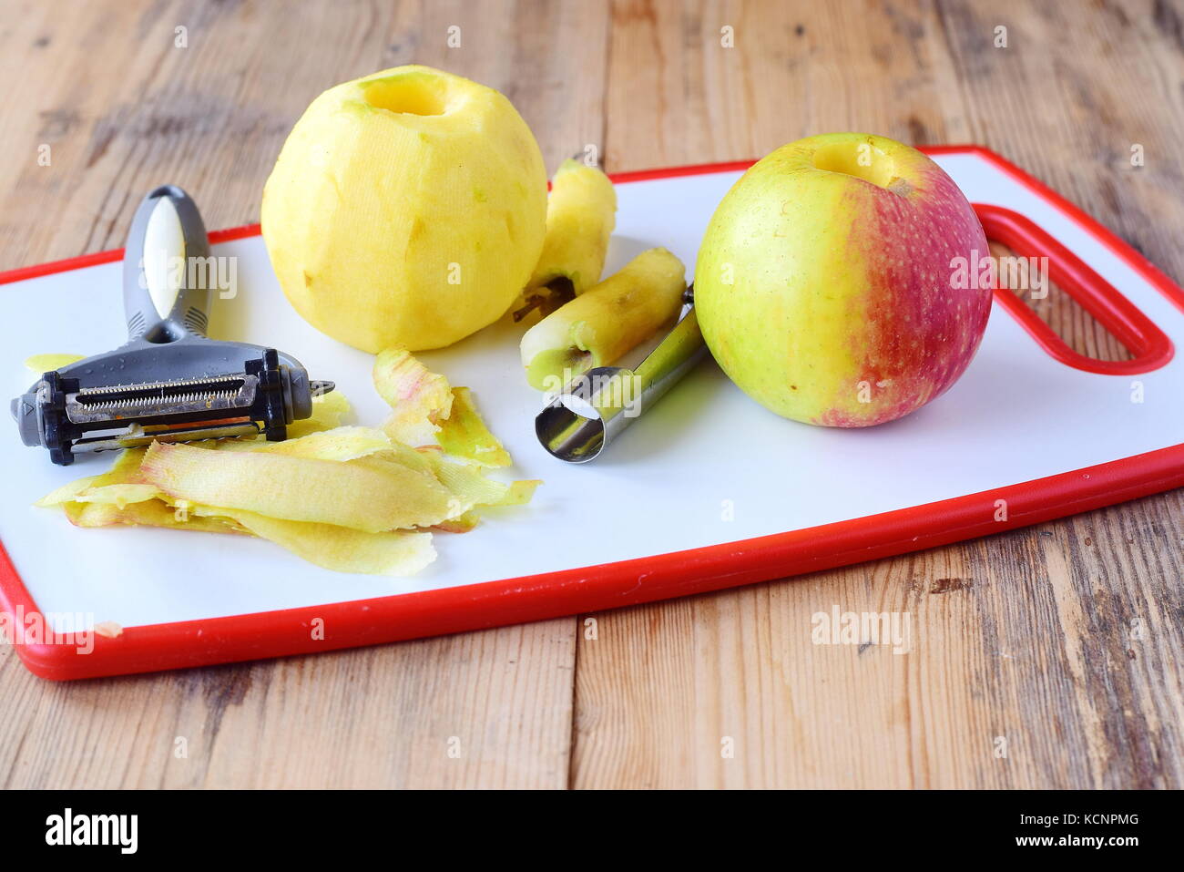 Geschälte Äpfel mit dem Kern entfernt mit speziellen Messern auf einem weißen Schneidbrett auf einer hölzernen Hintergrund genommen. Schritt für Schritt gesund Essen kochen. Stockfoto