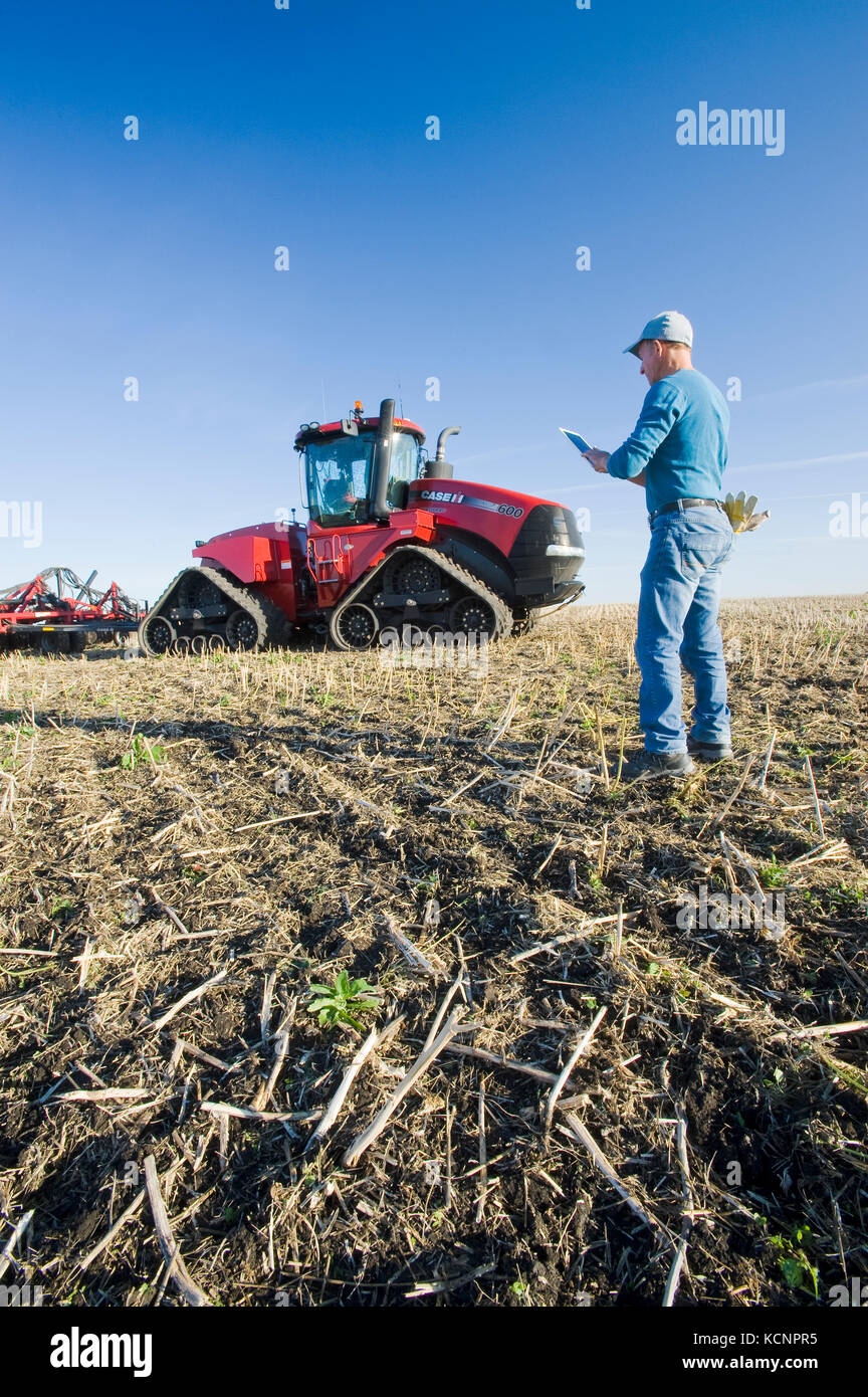 Landwirt mit einem Tablet vor einem Traktor und der pneumatischen Sämaschine, die Anpflanzung von Winterweizen in einem Null bis Feld mit Raps Stoppeln, in der Nähe von Lorette, Manitoba, Kanada Stockfoto