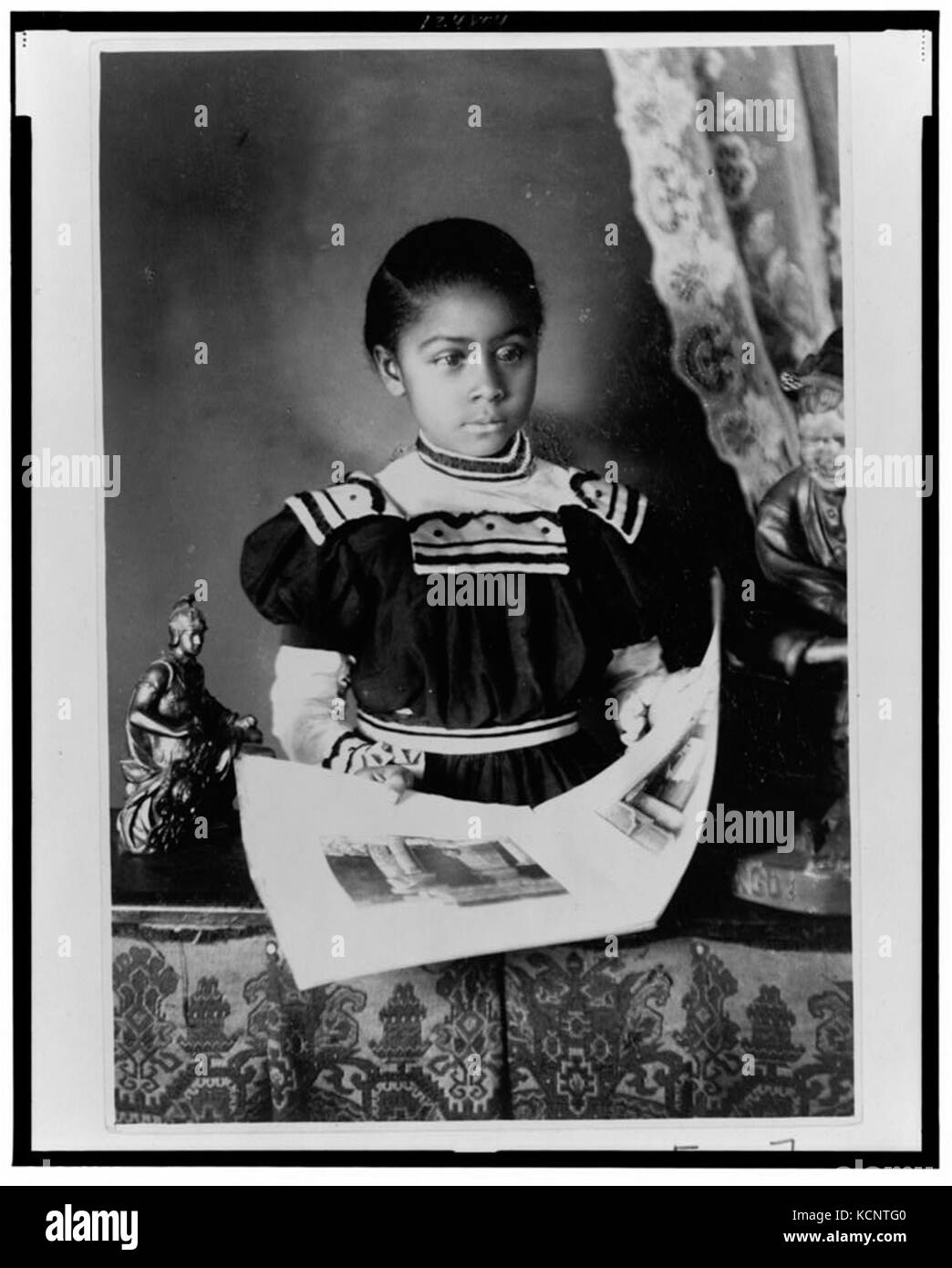 African American Girl, Brustbild, stehend am Tisch mit illustrierten Buch, mit leicht nach rechts LCCN 99472198 Stockfoto