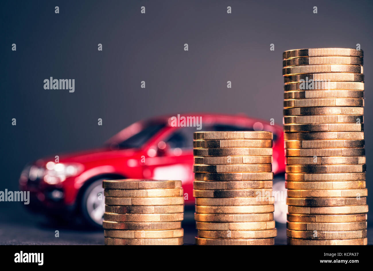 Steigende Stapel von Münzen und ein rotes Auto im Hintergrund Stockfoto