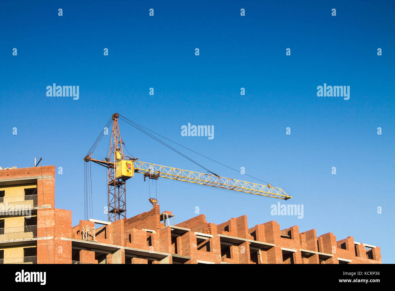 Ein gelber Kran baut ein Wohnhaus aus rotem Backstein Stockfoto