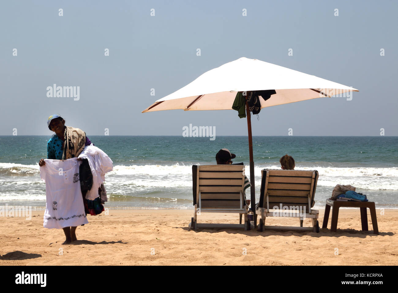 Bentota Sri Lanka Paar am Strand unter einem Sonnenschirm und hawker Verkauf tops Stockfoto