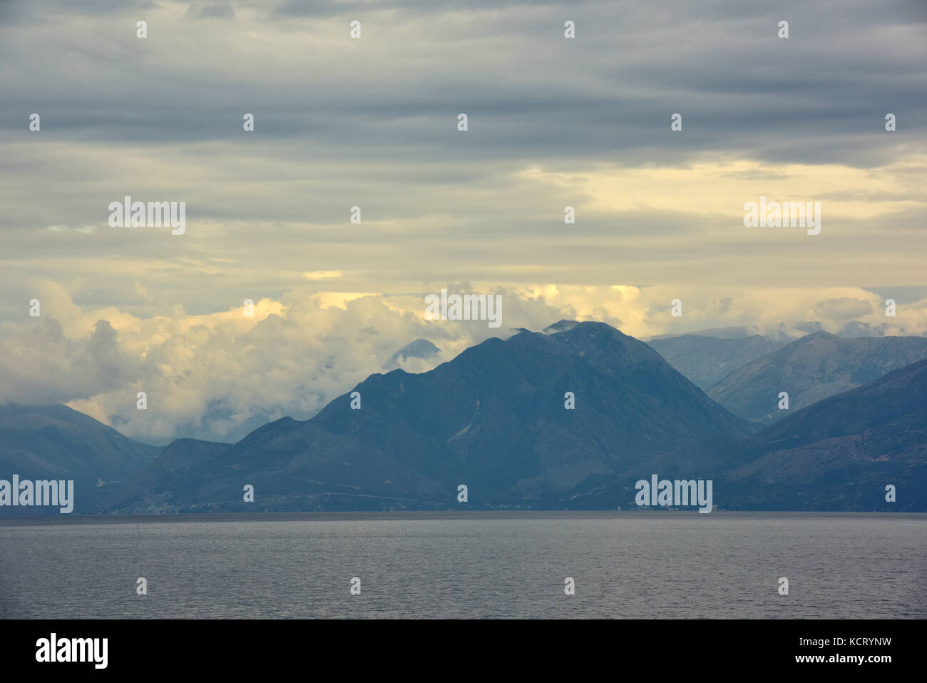 Die Berge und Hügel von Albanien gesehen von der Küste von Korfu angezeigt oder mit einem bewölkten bedrohlich brütende unruhigen grauen Himmel. wechselhafter Witterung. Stockfoto