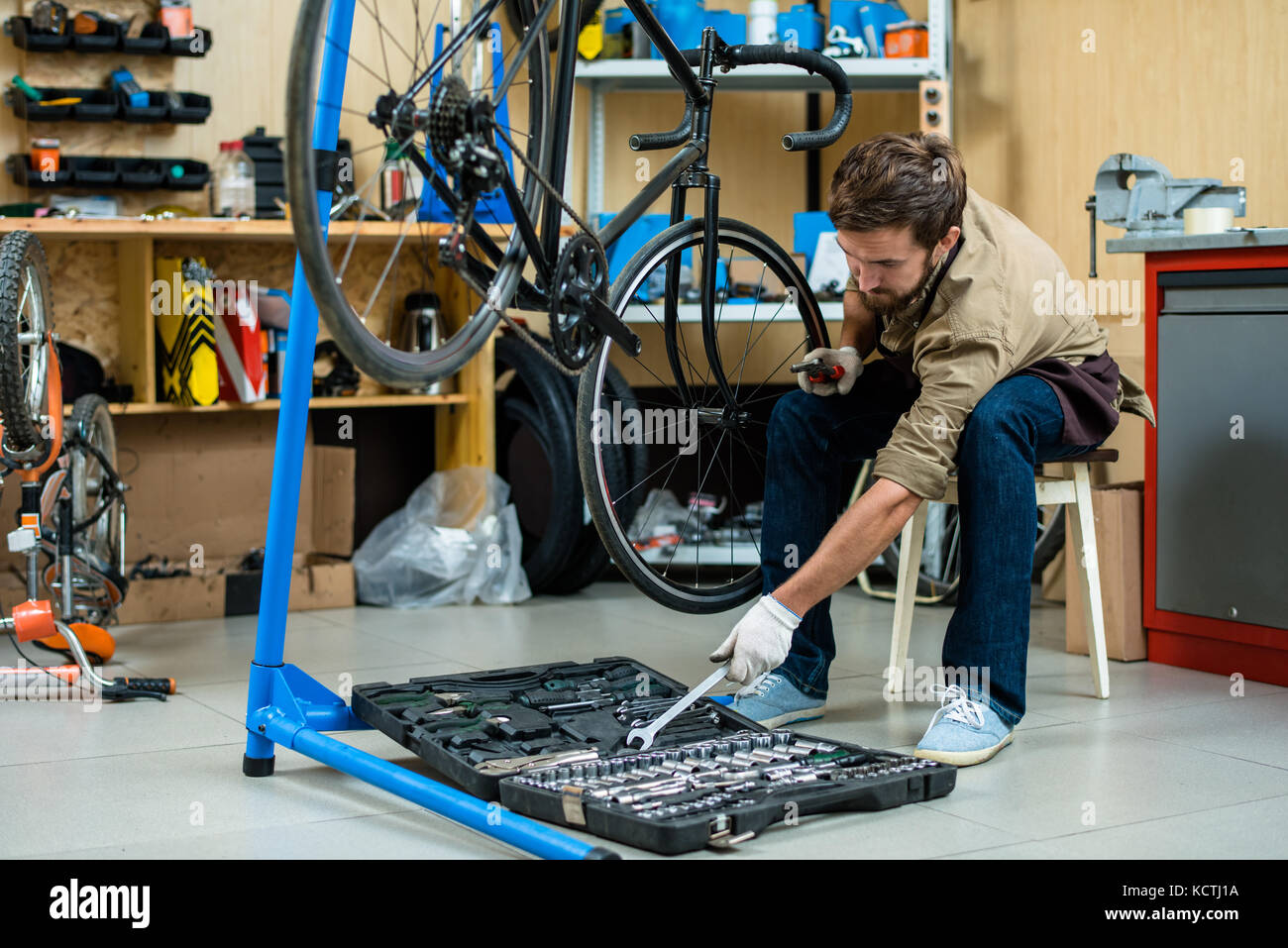 Junge Mechaniker unter Handwerkzeug von Toolkit während der Reparatur der Zyklus Rad Stockfoto