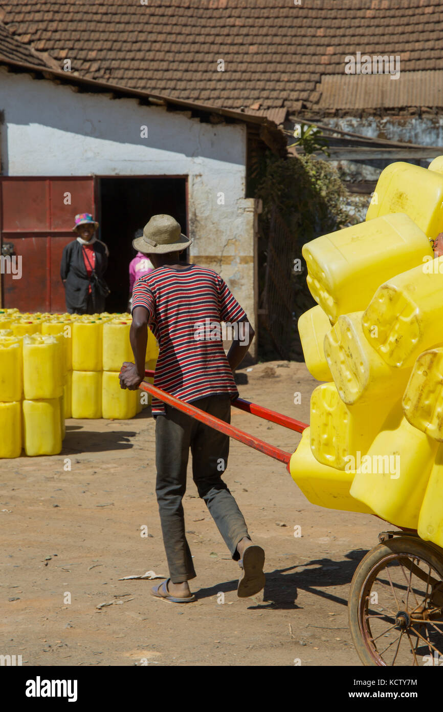 Mann ziehen Rikscha mit leuchtend gelben Kunststoff Fässer, Antsirabe, Madagaskar, 2017 geladen Stockfoto