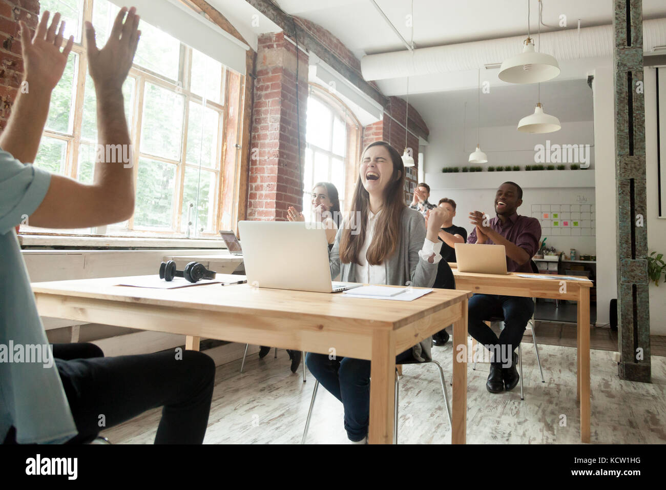 Multiethnische Team von Mitarbeitern feiern gewaltige Leistung in Shared Office. Happy girl in Freude schreien, Rest der Kollegen klatschen um Sie herum Stockfoto