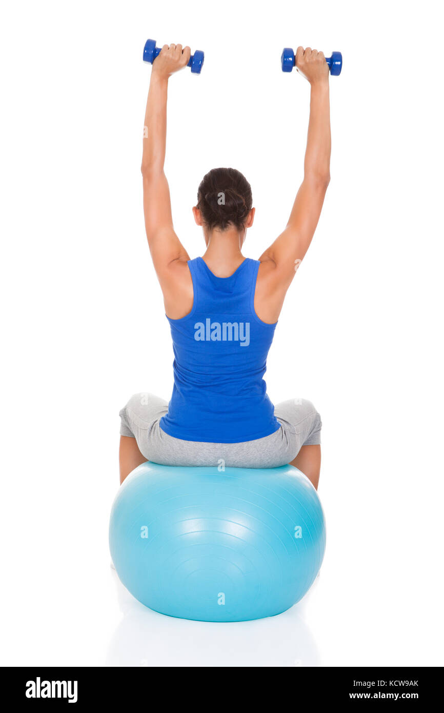 Junge Frau, die das Training mit Hanteln am blauen Fitnessball Over White Background Stockfoto