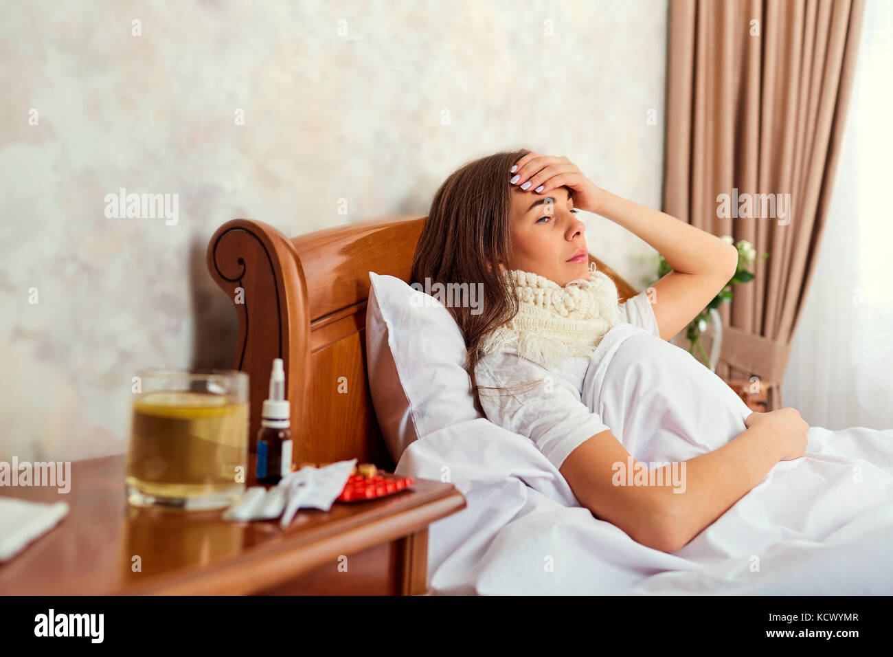 Eine kranke Frau mit Temperatur liegt im Bett. Stockfoto