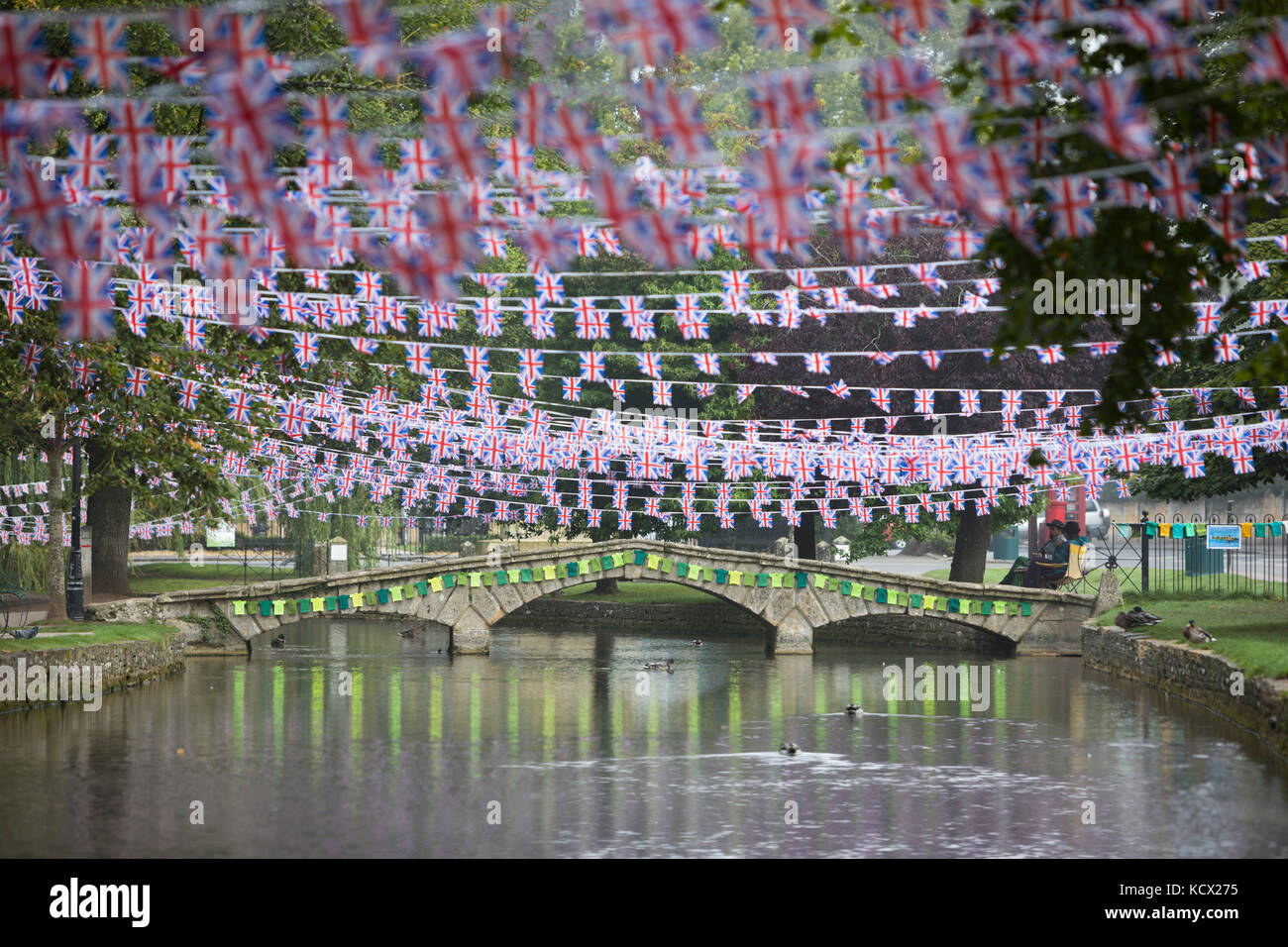 Steinerne Brücke über den Fluss Windrush mit gestrickten Radfahren Westen und Union Jack Flags für die Tour von Großbritannien Radrennen eingerichtet Stockfoto