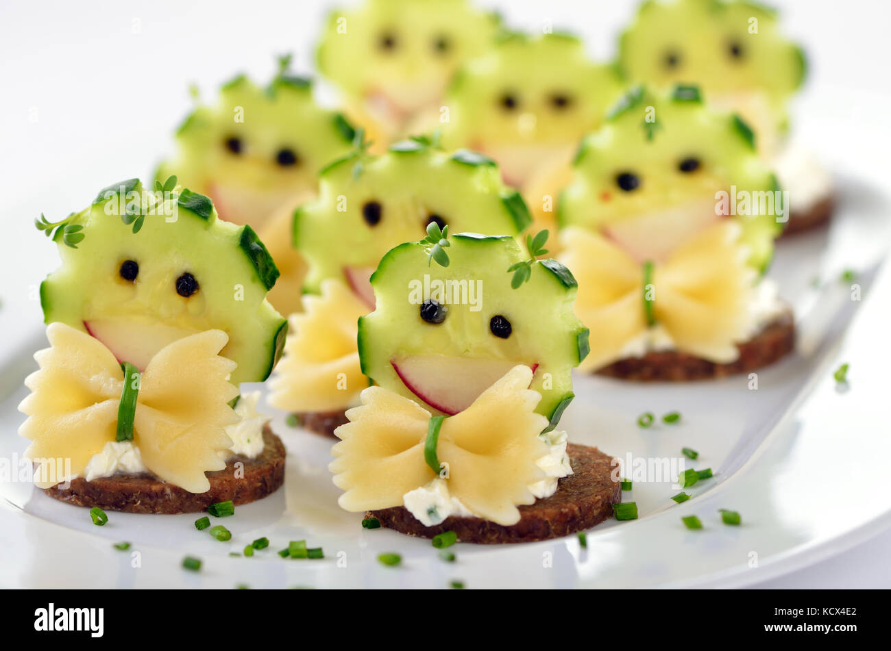 Lustige Snacks mit würziger Frischkäse, dekoriert mit Gurke, Radieschen ...