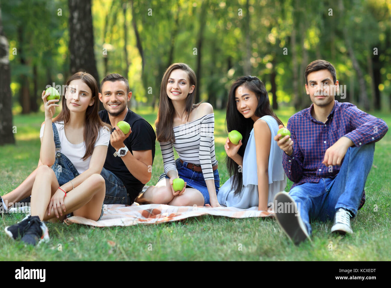 Portrait von Fröhlichen Freunden halten grüne Äpfel sitzen auf Gras. ein gesunder Lebensstil, Ernährung, Jugend und schöne junge Menschen glücklich Konzept Stockfoto