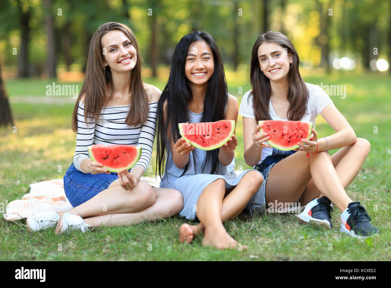 Portrait von drei schöne Frau mit Scheiben Wassermelone im Freien. ein asiatisches Mädchen und zwei kaukasischen Spaß im Picnic mit Obst auf warmen Tag. fr Stockfoto
