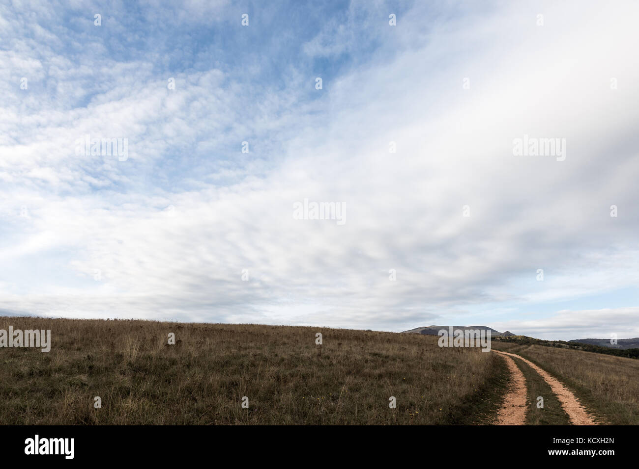 Eine kleine Landstraße unter grossen blauen Himmel und weißen Wolken Stockfoto