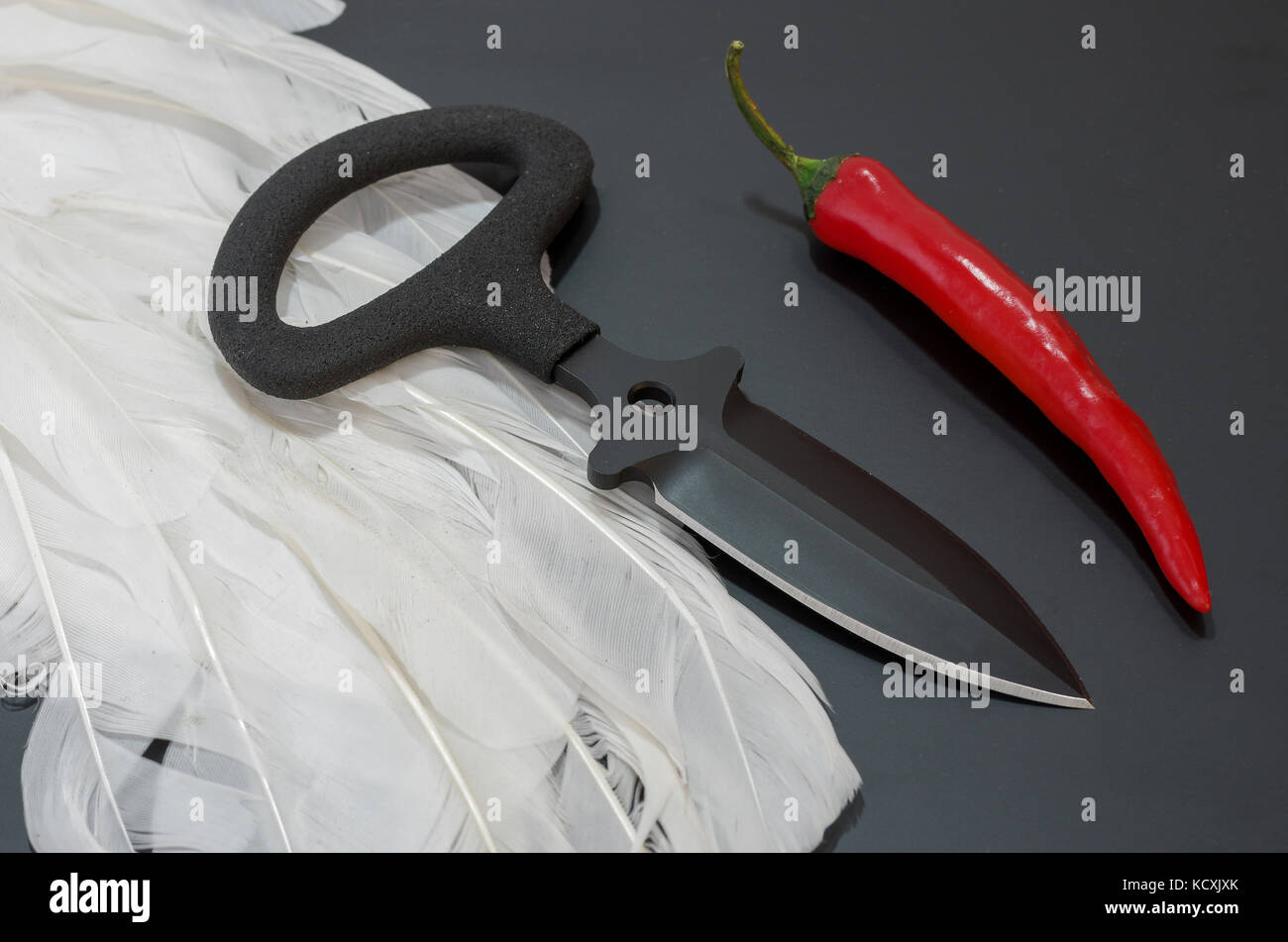 Schwarze Messer auf einem schwarzen Hintergrund. Weiße Federn und rotem Pfeffer. Taktisches Konzept. Stockfoto