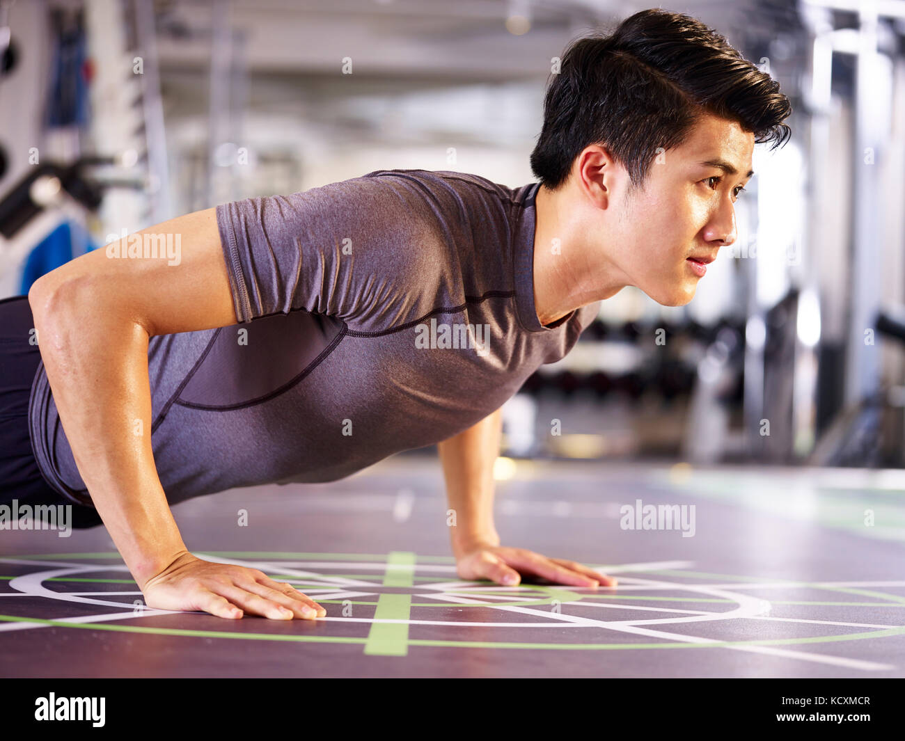 Jungen asiatischen erwachsenen Mann das Trainieren im Fitnessstudio tun Push-ups, Seitenansicht. Stockfoto