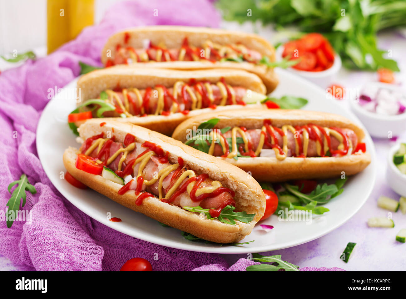 Hot Dog mit Wurst, Speck, Gurken, Tomaten und Zwiebel rot auf weiß Platte Stockfoto