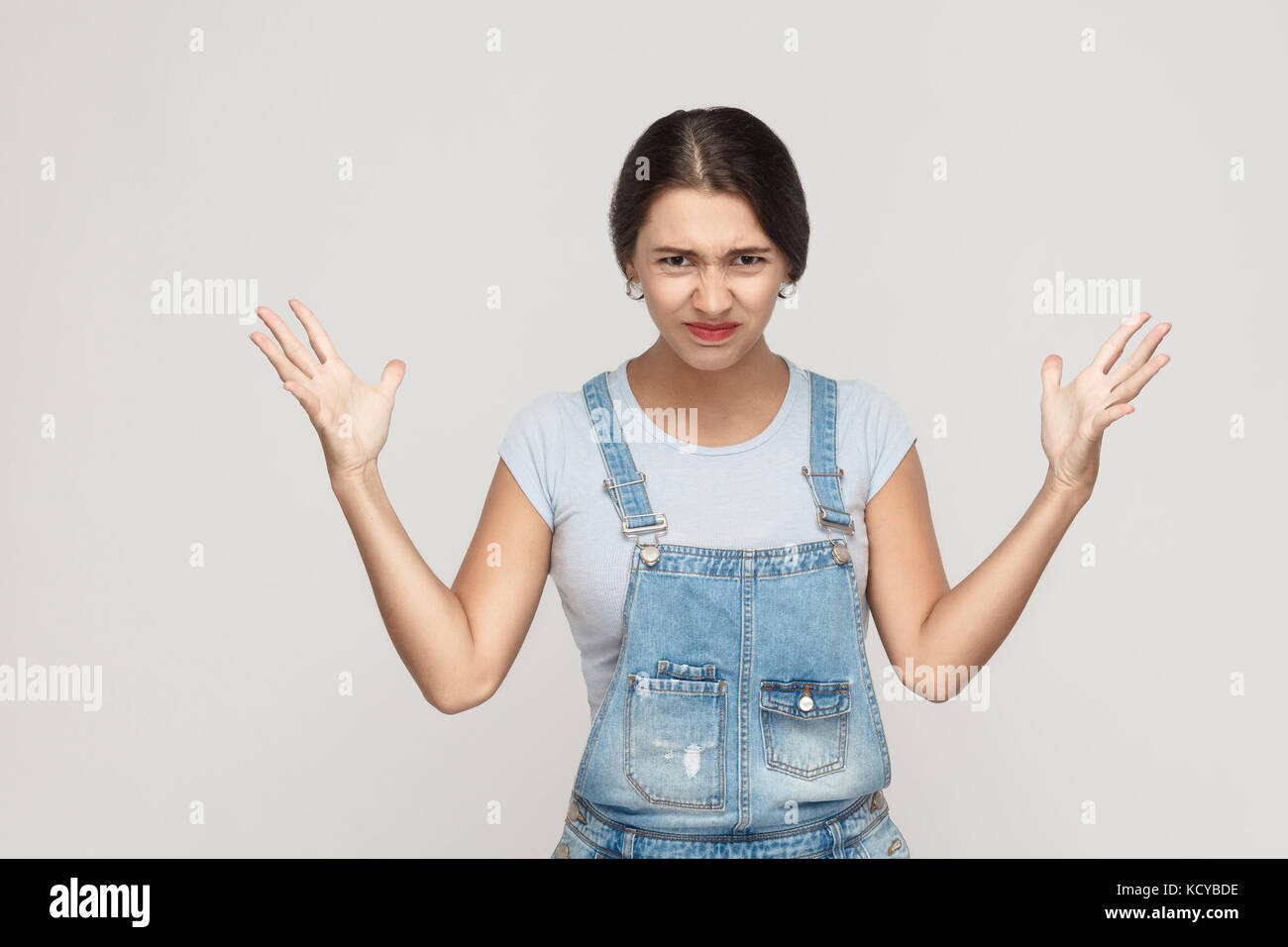 Zorn spanische Frau in Verzweiflung und Schock. Portrait von jungen Erwachsenen wütende Frau in Blau denimoveralls, Panik in Kamera mit Mund weit geöffnet, wi Stockfoto