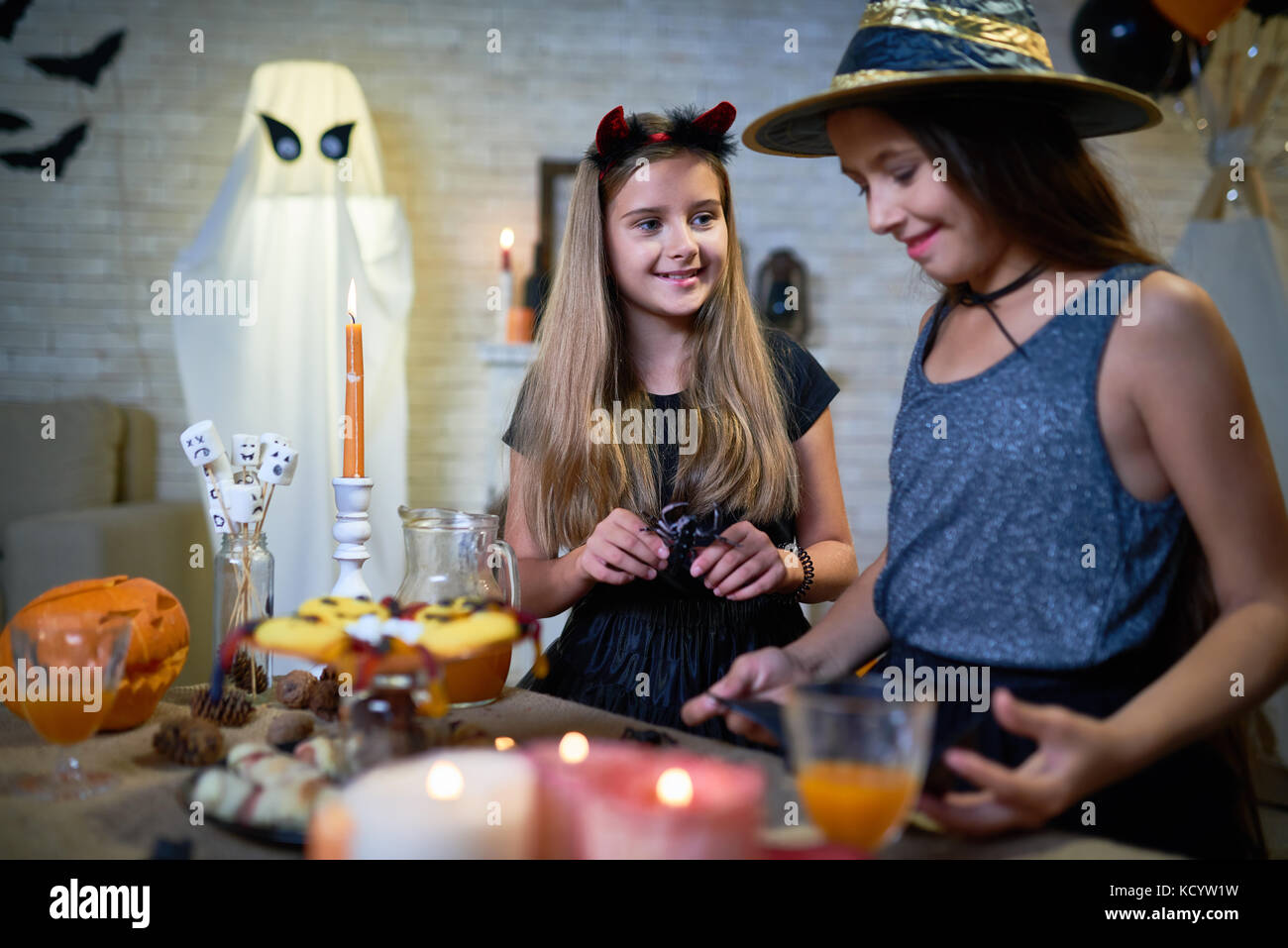 Portrait von zwei jugendlichen Mädchen, die Hexe Kostüme Einrichten snack Tabelle an Halloween Party in eingerichtete Zimmer Stockfoto