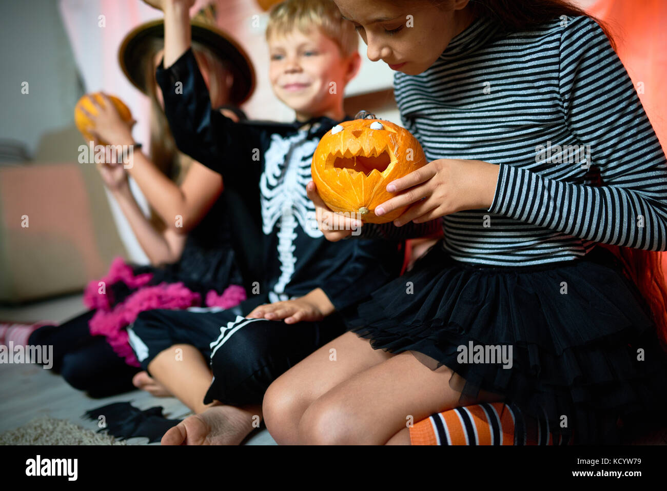 Closeup Portrait von drei Kindern tragen Halloween Kostüme sitzen auf dem Boden im Zimmer, auf Mädchen mit kleinen geschnitzten Kürbis Fokus Stockfoto