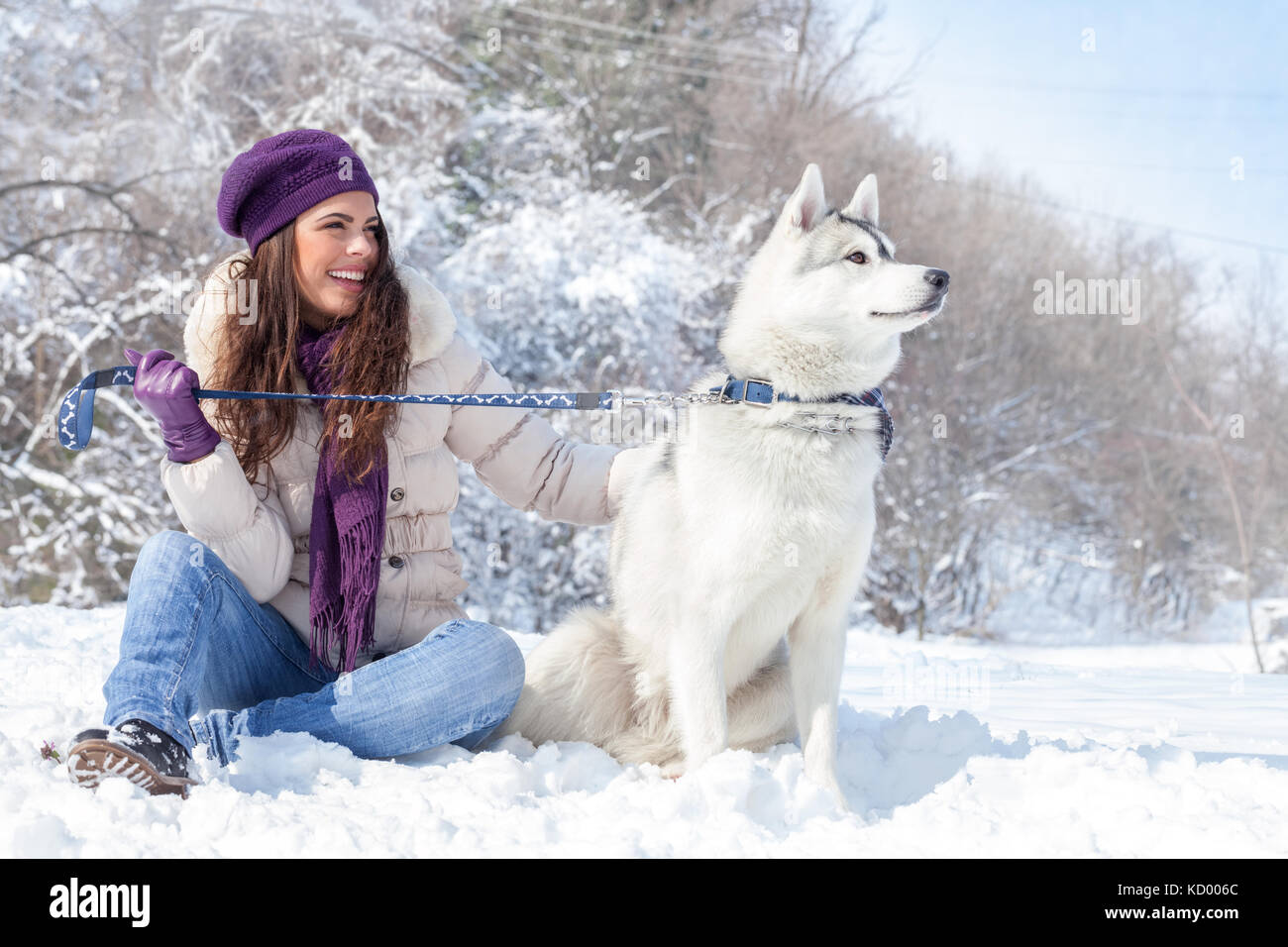 Junge schöne Frau sitzt mit Husky Hund im Winter Forest Stockfoto