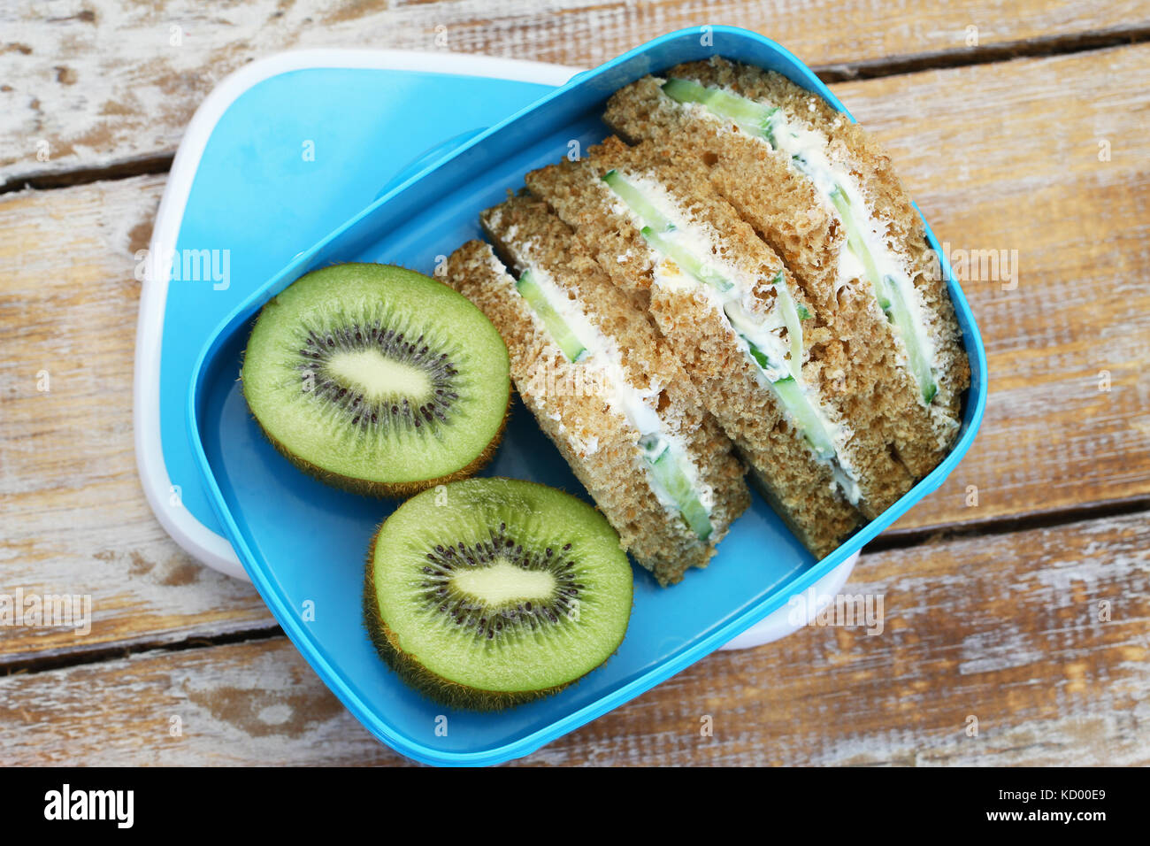 Braunes Brot Sandwiches mit Frischkäse und Gurken und Kiwi in blau Lunch Box Stockfoto
