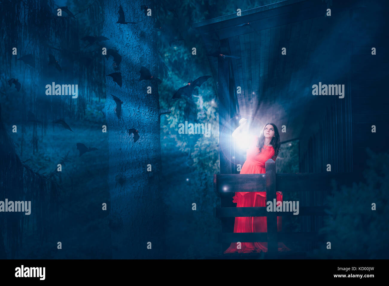 Fantasy Foto mit einer schönen Frau im roten Kleid, mit einem Holzhaus in einem dunklen Wald, halten eine Laterne mit Lichtstrahlen entfernt die Fledermäuse zu jagen Stockfoto